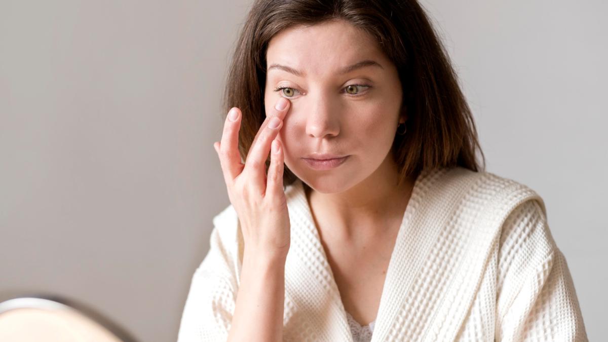 Женщина наносит крем под глаза