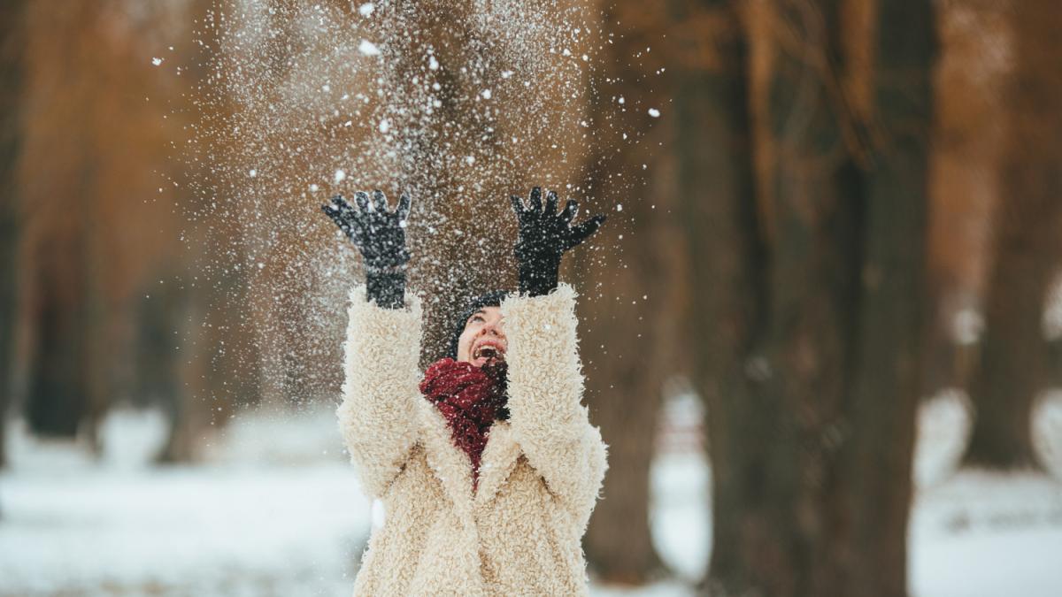 Молодая красивая женщина бросает снег над головой